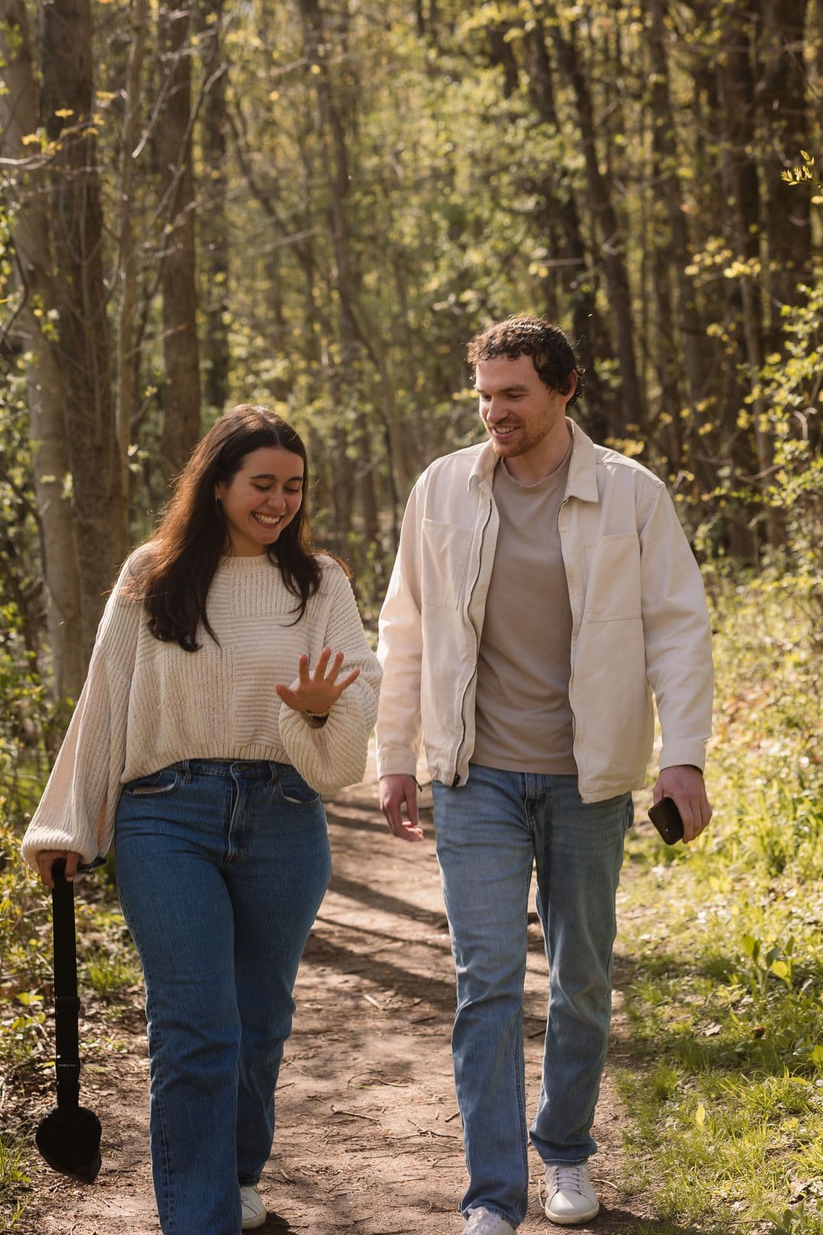 A newly engaged couple walking a wooded trail admiring the ring