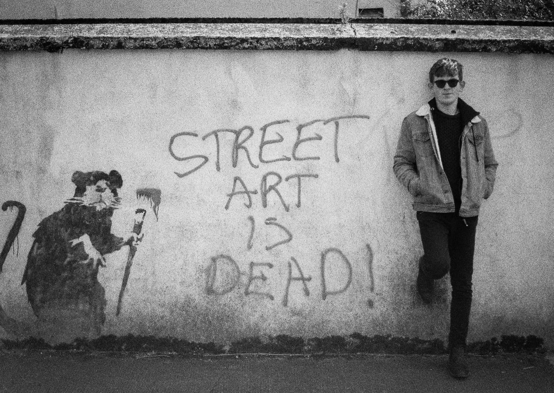 film photo person leaning against wall with banksy graffiti