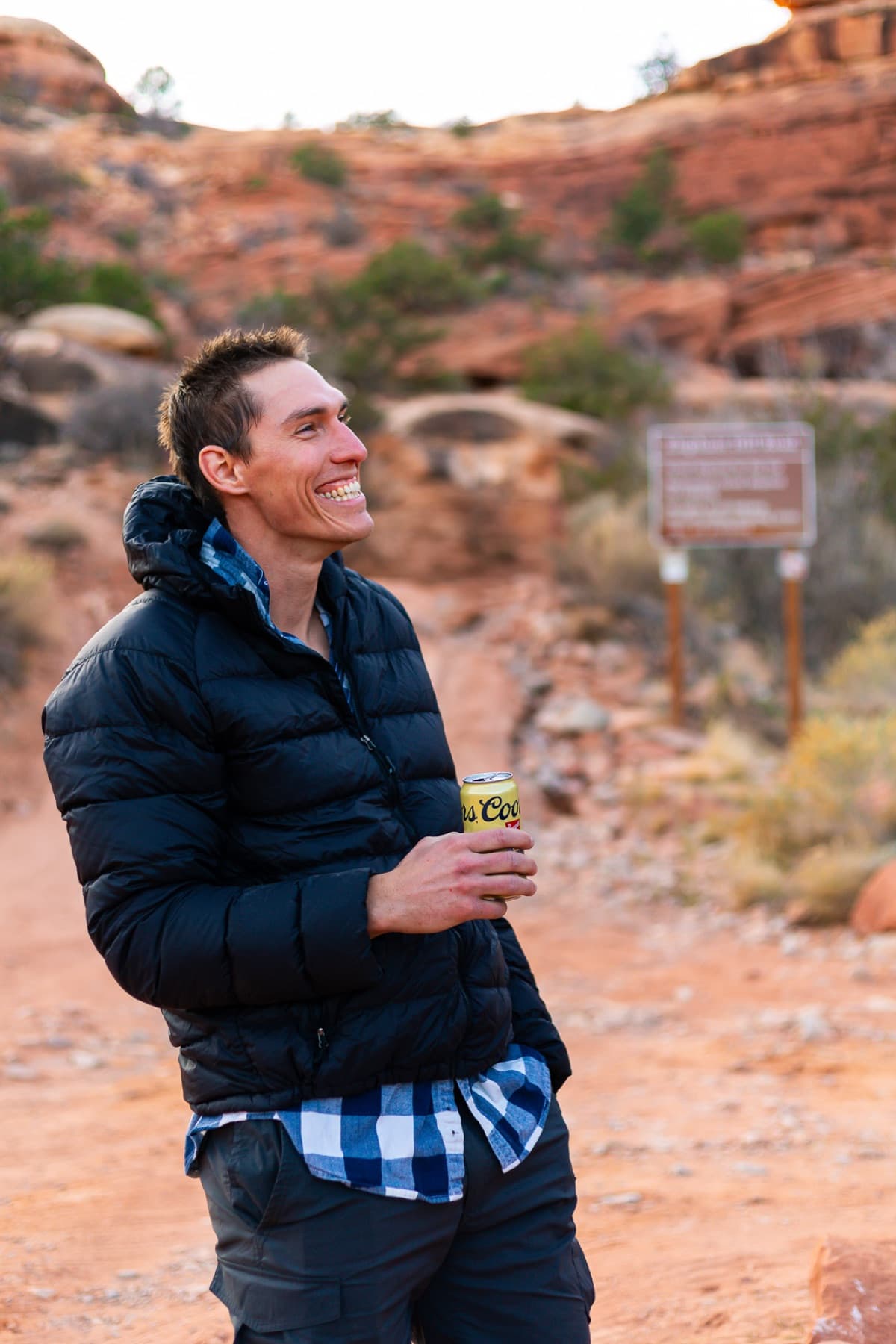 A happy camper smiling with a beer in hand among red rocks
